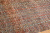 Distressed Belouch rug texture showcasing repeating geometric florals in dusty blue and chestnut.