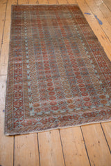 Distressed Belouch rug corner featuring geometric wave motif in dusty blue and chestnut.