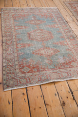 Angled view of a distressed vintage rug highlighting the worn, low pile and faded red and blue design.