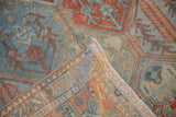 Folded corner of a distressed Bakhtiari rug reveals its hand-knotted back and worn, low pile.