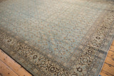 Angled view of a distressed Tabriz carpet corner, contrasting the ivory border with the denim blue Herati field.