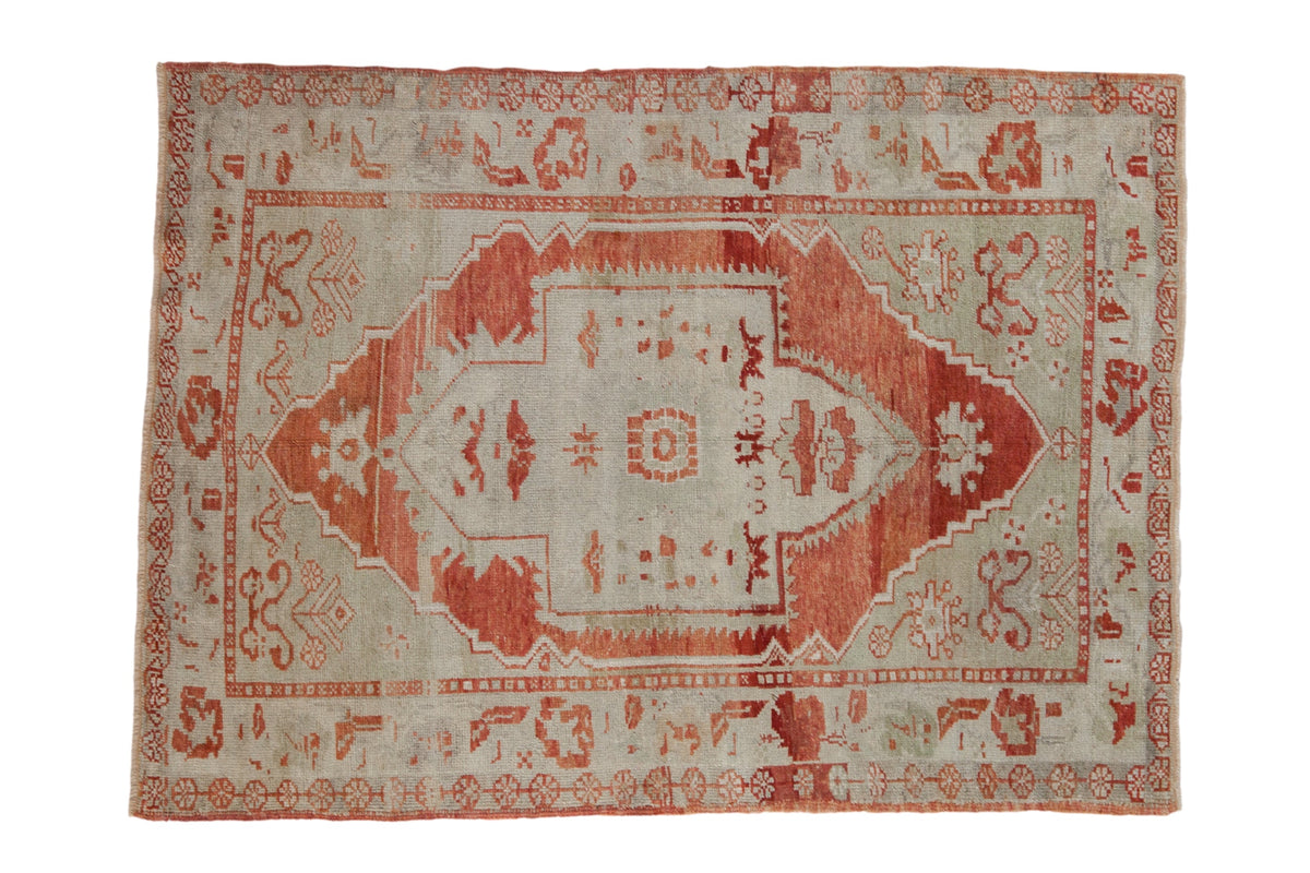 Vintage distressed Oushak rug with a red shield medallion on an abrashed seafoam green field.