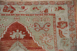 Worn, hand-knotted pile on a vintage Oushak corner with red, ivory, and seafoam green patterns.