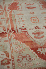 Close-up on the distressed Oushak's hand-knotted texture and low pile in cherry red and ivory.