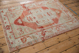 Distressed Oushak rug from an angle, highlighting its red shield medallion and seafoam green field.