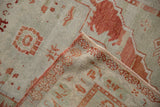 A folded corner displays the even, low pile and hand-knotted reverse of a distressed Oushak rug.