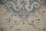 Close-up of stylized people, animals, and snowflake motifs on a distressed Caucasian rug.