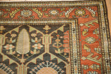 Corner detail of a fine Persian rug with cypress tree motifs and a geometric floral border in rust and charcoal.