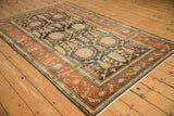 A vintage Mehriban rug's charcoal lattice field and rust border seen from a full-length angled view.