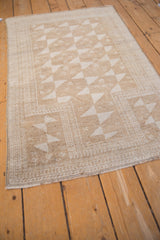 Corner detail of distressed vintage Belouch rug, featuring geometric pinwheels, soft beige, and worn foundation.