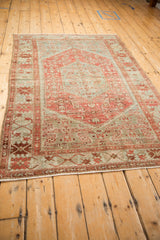 Angled view of the vintage Malayer rug with its faded raspberry red and dusty blue design.