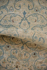 Rolled vintage Distressed Tabriz rug with blue arabesque vines and exposed foundation.