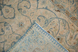 Distressed Tabriz rug folded, showing worn blue scrolling vines and light foundation with selvage.