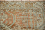 Corner of a distressed Malayer rug showing a meandering serrated vine border in terracotta and powder blue.