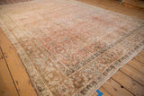 Angled view of a vintage Bijar carpet's faded blush floral field and complex sand-toned border.