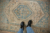 Looking down at the distressed texture of a vintage Hamadan rug with a dusty blue medallion.