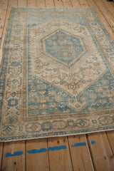 Angled view of a distressed vintage Hamadan rug with a sky blue and beige geometric pattern.