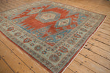 Angled view of a square Persian Veece rug with distressed cherry red and sapphire blue medallions.
