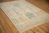 A distressed Oushak rug's full pattern in sand and denim blue tones, viewed at an angle.