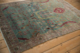 Angled view of a distressed Persian rug showing bird motifs on a dusty blue-green field.