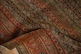 Folded texture of the antique Senneh rug, revealing faded red, brown, and ivory vine patterns.