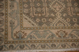 Detailed view of the corner on a distressed Hamadan rug showing geometric borders and soft ivory fringe.