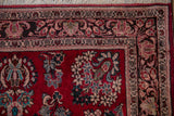 Corner detail of a vintage Sarouk rug featuring cherry red field, turquoise floral sprays, and dark borders.