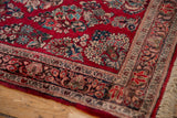 Vintage Sarouk rug corner displaying cherry red field, floral border, and fringe.