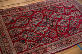 Vibrant cherry red field with turquoise and beige floral sprays, showing ornate Sarouk rug border.
