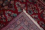 Corner of vintage Sarouk rug with cherry red floral field and intricate blue-red border.
