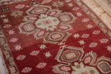 Low-pile texture showing crab-style motifs and starburst flowers on a rust-colored Caucasian rug.