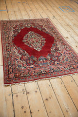 Vintage Sarouk rug seen from an angle, showing its red diamond medallion and floral borders.