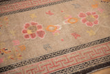 Antique Ningxia rug detail showing pink running-T border and worn beige field with floral motifs.