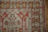 Corner view of a distressed Anatolian rug showing coffee brown borders with saffron and red motifs.