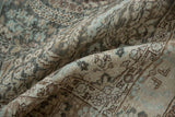 Softly worn, low-pile texture of a distressed Tabriz rug in dusty teal, silver, and beige tones.