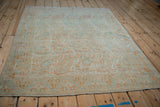 Vintage distressed Persian rug showing soft wear and a pastel boteh design from an angle.