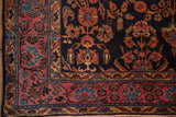 Detailed corner showing the raspberry red palmette border and navy blue floral field of an antique Sarouk rug.