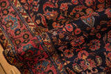 Plush pile of a folded antique Sarouk rug with a navy floral field and raspberry red border.