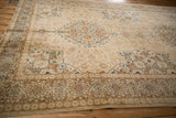 Corner view of a distressed Tabriz carpet's floral cartouche border and ivory field.