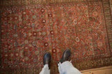 An antique Malayer rug's abrashed rust field displaying a geometric Herati design in blue and beige.