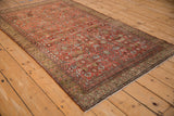 Angled view of an antique Malayer rug highlighting its chestnut Herati field and henna design border.