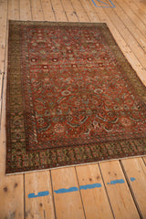 Angled view of an antique Malayer rug, showcasing the rust-red geometric field and olive border.