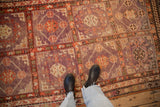Distressed vintage Khotan rug with pale aubergine and faded red geometric panels viewed from above.