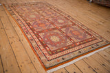Angled view of the distressed Khotan rug's repeating aubergine and red panels.