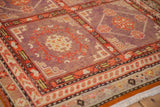 Geometric blossom motifs within the aubergine and red lattice panels of a distressed Khotan rug.
