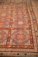 Angled view of a distressed Khotan rug showing its low pile texture and faded aubergine panels.