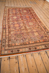 Angled view of a distressed Khotan rug's lattice pattern in faded aubergine, violet, and tomato red hues.