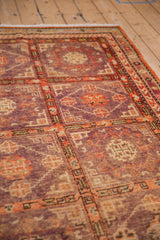 Angled view of a distressed Khotan rug's low pile and geometric lattice pattern in aubergine and faded red.