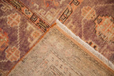 Folded corner of a distressed Khotan rug showing the hand-knotted foundation and aubergine wool pile.