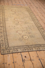 An angled perspective of the antique Karabagh rug highlights its distressed field and scattered pictorial motifs.